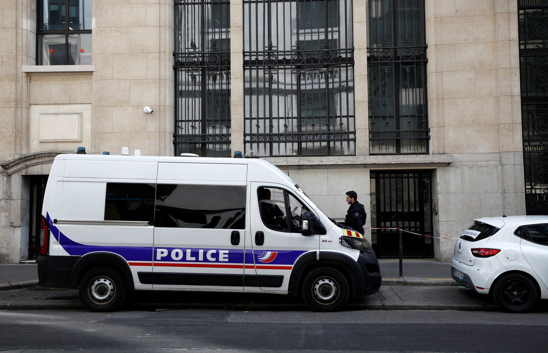 A policeman stands alongside police and private security vehicles outside The Bank of America building in the 8th arrondissement of Paris on March 28, 2026