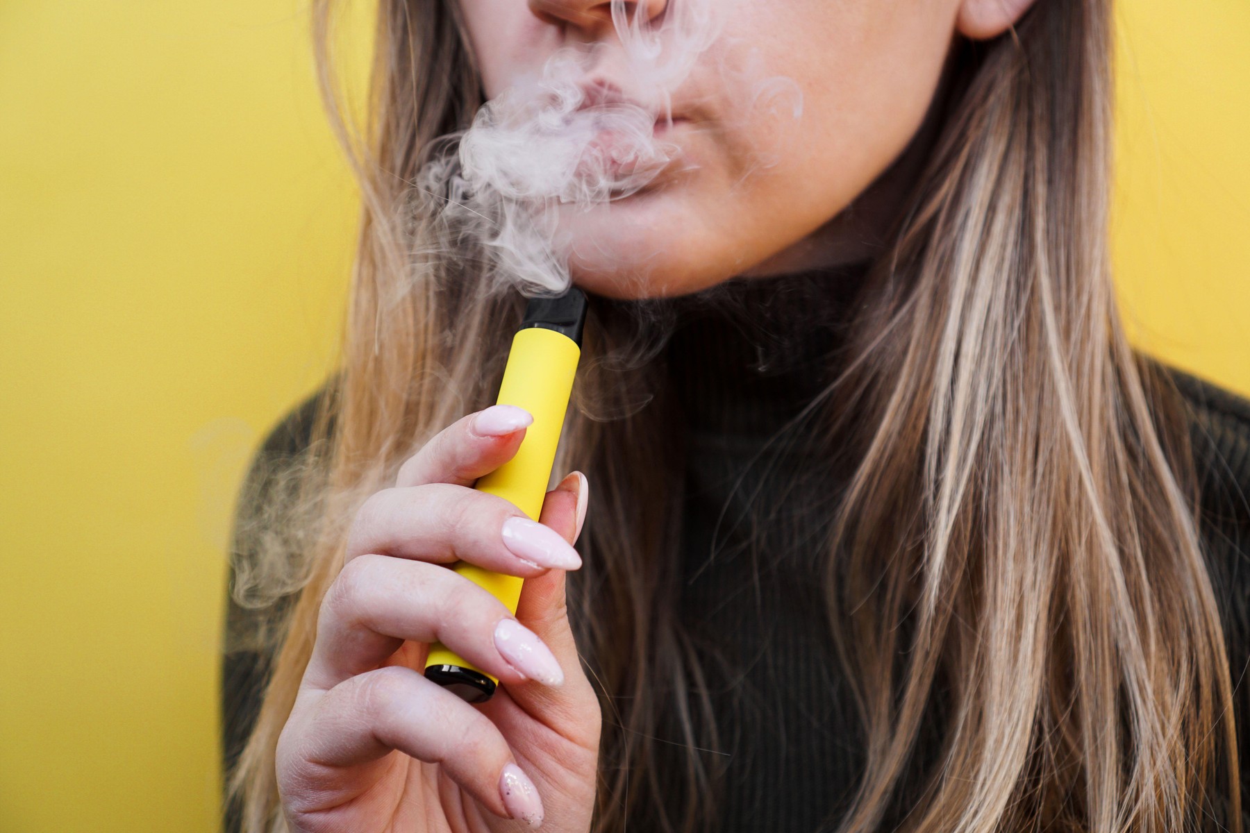 Close up of a young girl smokes a disposable electronic cigarette and exhales smoke.