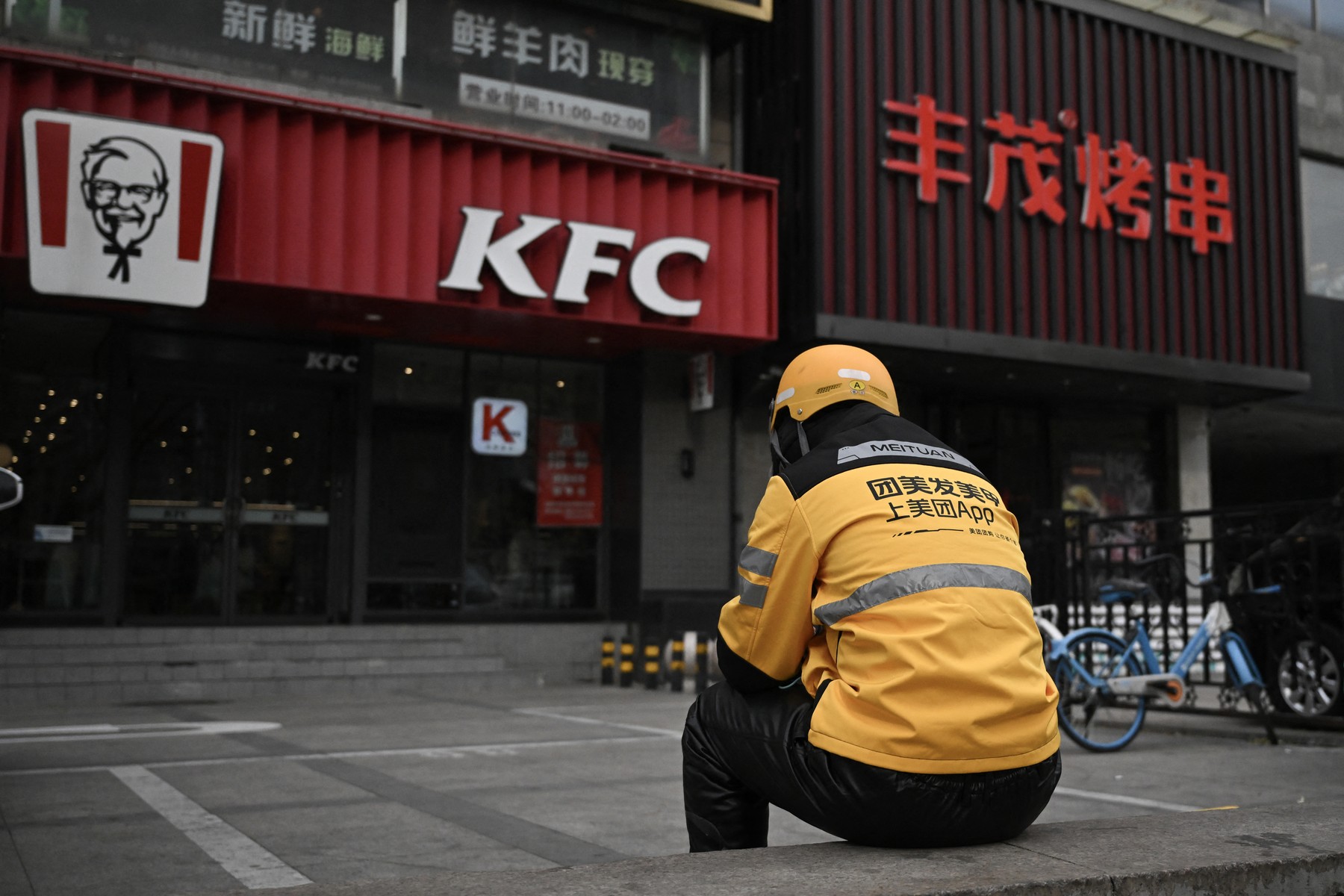A food delivery man for Chinese company Meituan waits for orders outside a KFC branch in Beijing