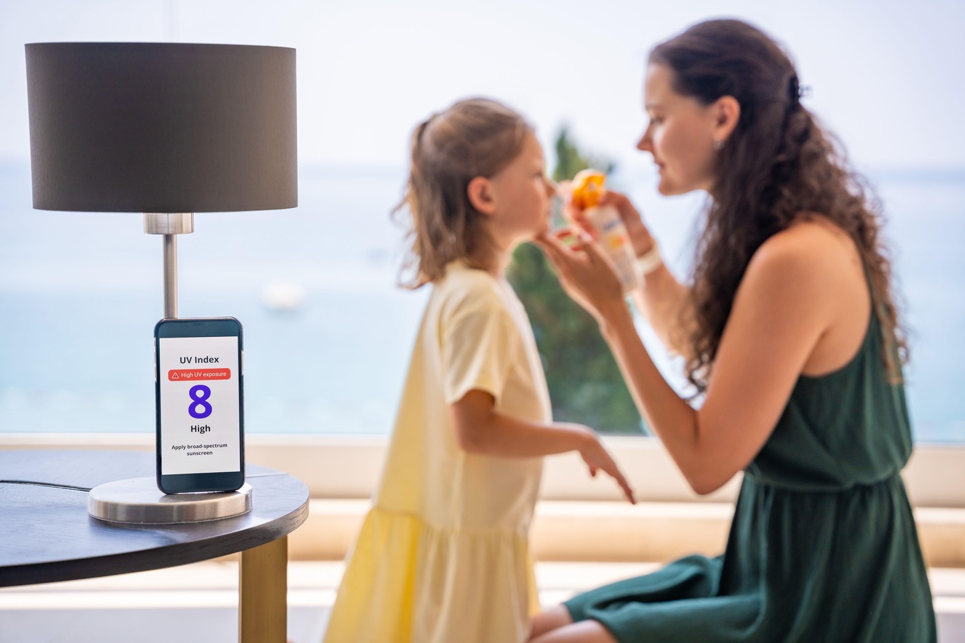 pametni telefon z UV indeksom in mama, ki z zaščitno kremo maže hčerko