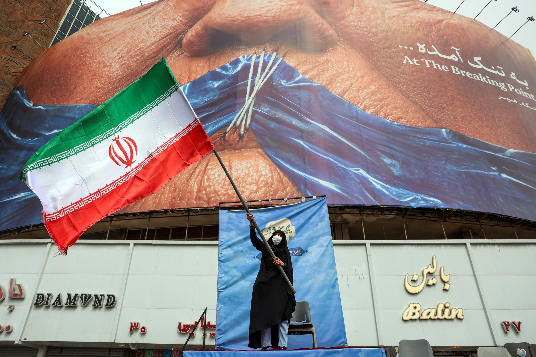 A woman waves an Iranian flag in front of an anti-US billboard referring to US President Donald Trump and the Strait of Hormuz at Valiasr Square in Tehran on May 5, 2026.