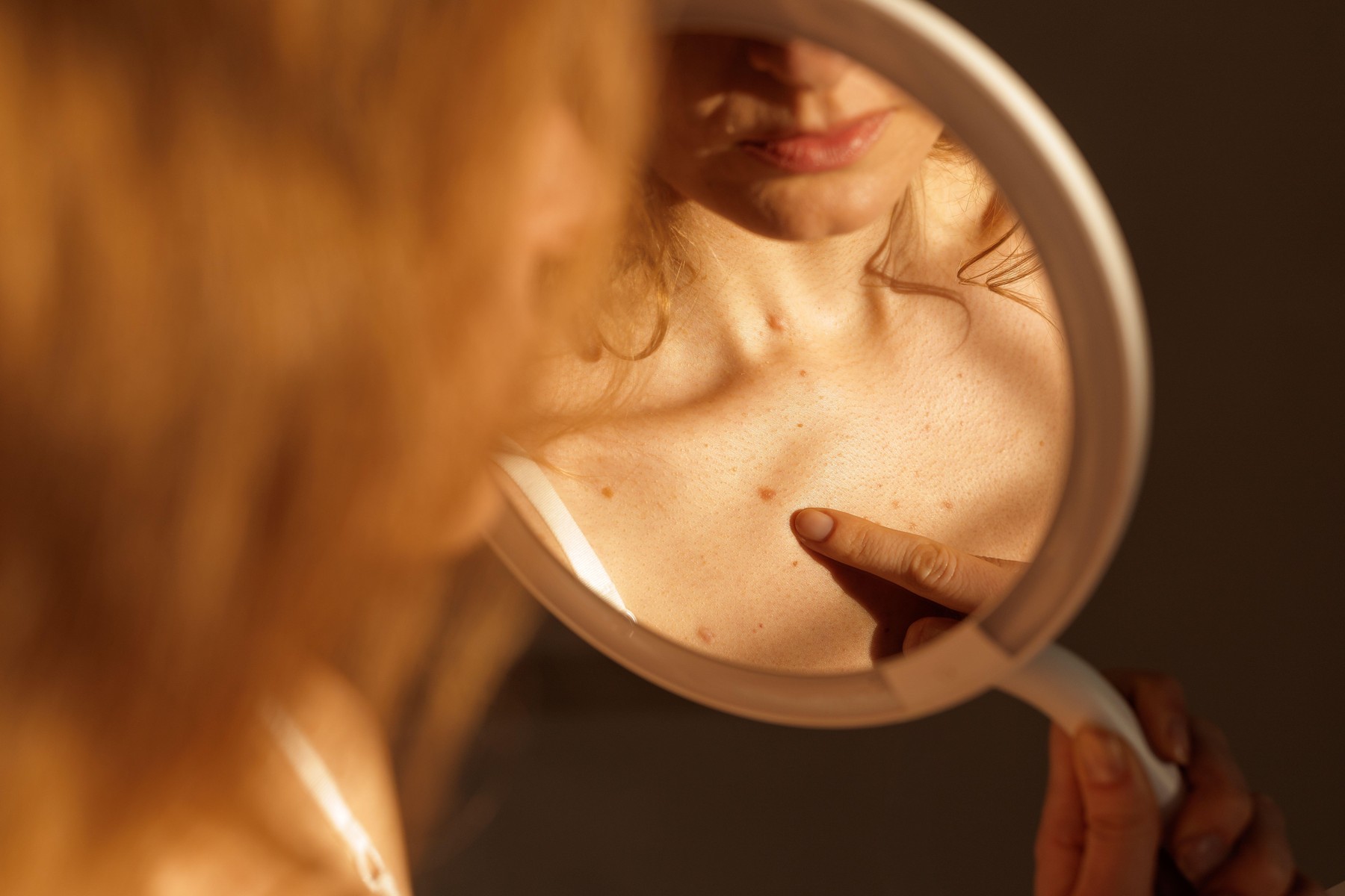 Close-up of woman examining mole on chest using mirror for self-check