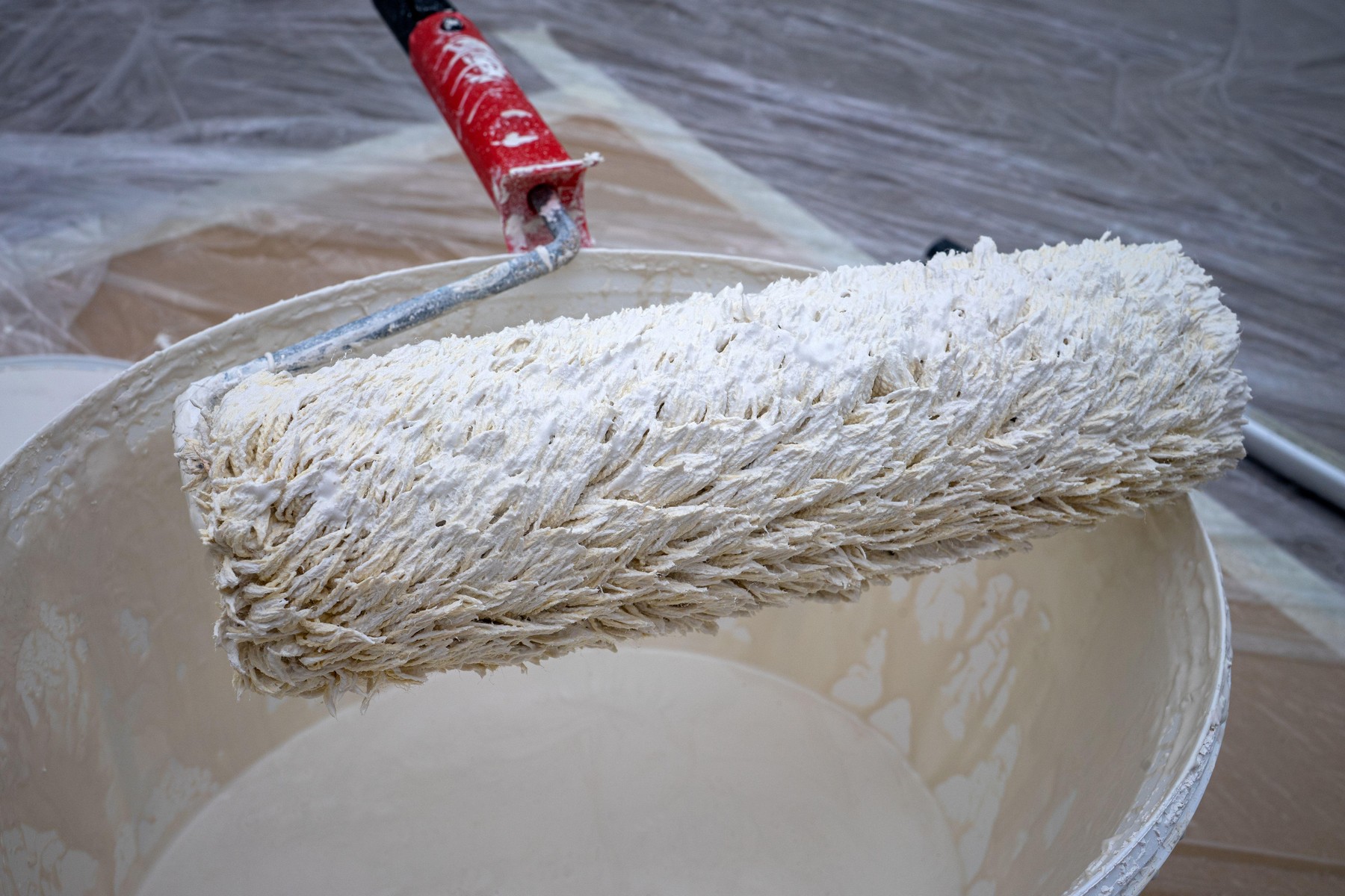 A person uses a paint roller to apply white paint from a bucket in an indoor space. The floor is covered to protect it from paint. The project is for home improvement.,Image: 1113491334, License: Royalty-free, Restrictions: , Model Release: no