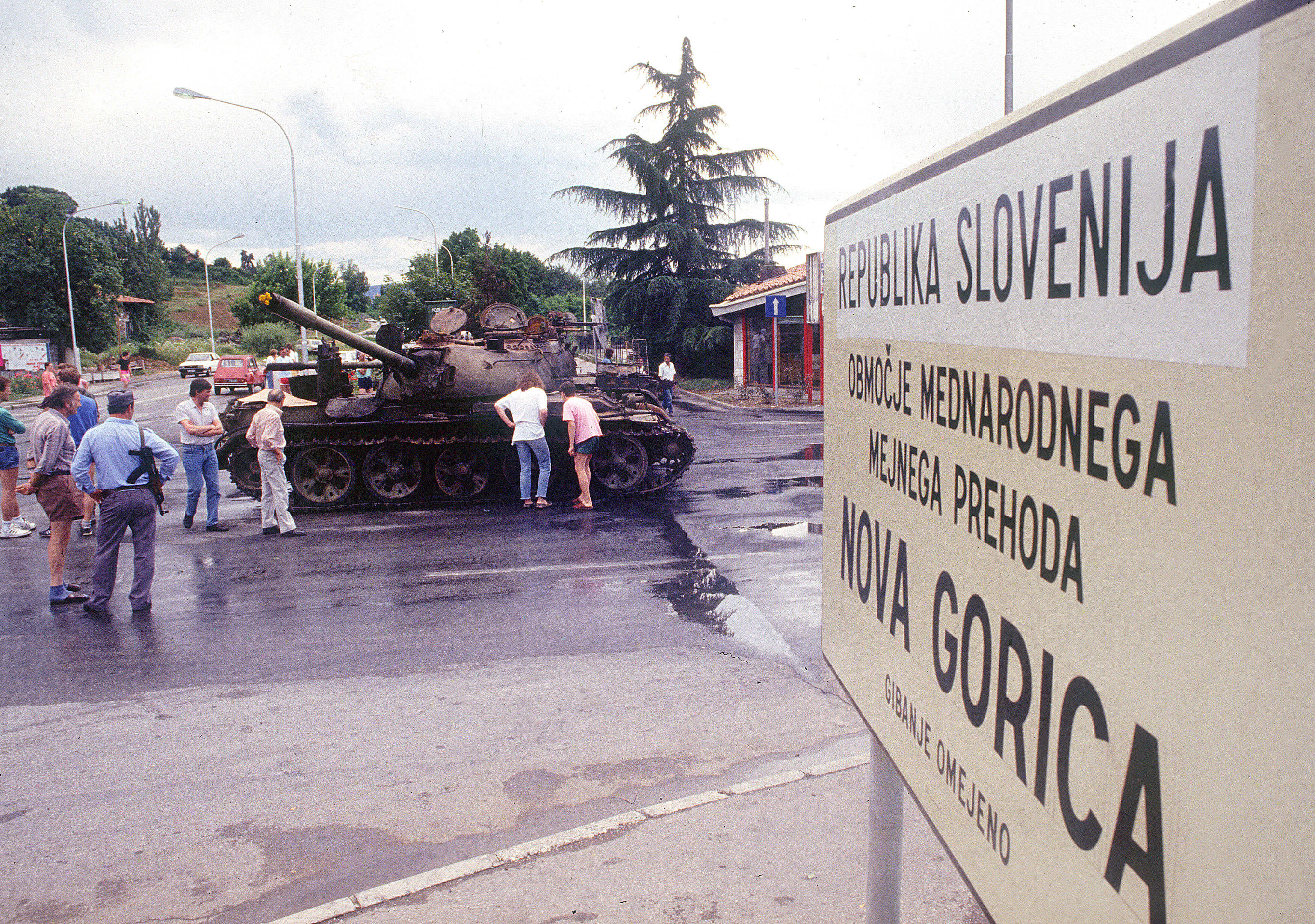 Ljudje gledajo dva požgana tanka JLA na mejnem prehodu v Rožni dolini
