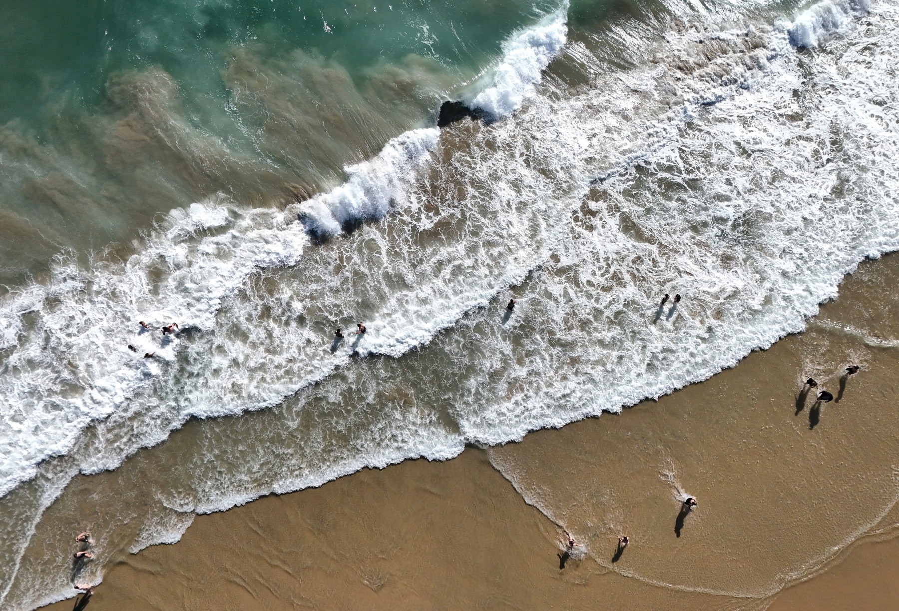 HUNTINGTON BEACH, CALIFORNIA - JULY 31: In an aerial view, people gather as Pacific Ocean waves break