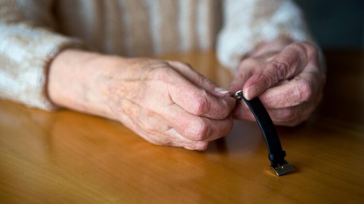 Roke starejše osebe, ki drži uro.