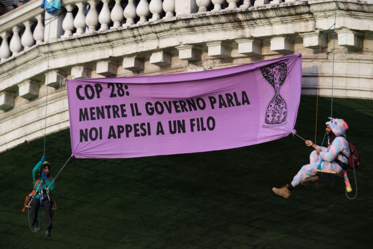 transparent z napisom: "COP28: Medtem ko se vlada pogovarja, mi visimo na nitki."