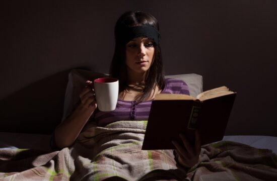 ženska v postelji s knjigo in skodelico pijače