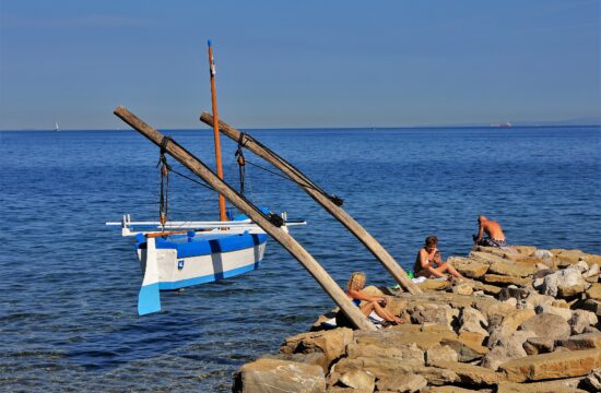 Turisti sedijo na plaži v Izoli