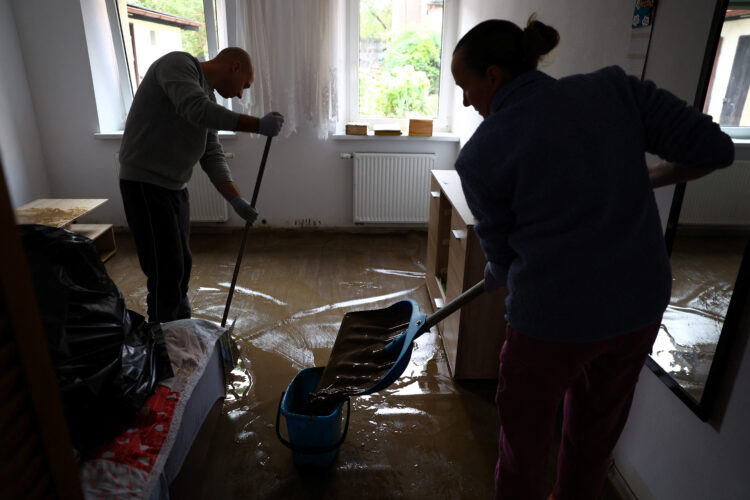 moški in ženska iz hiše spravljata vodo