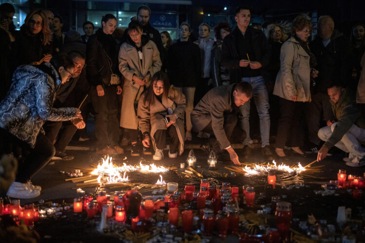 Ljudje prižigajo sveče in nosijo cvetje pred železniško postajo v Novem Sadu