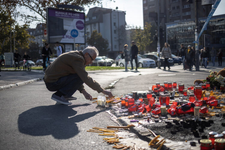 Ljudje prižigajo sveče in nosijo cvetje pred železniško postajo v Novem Sadu