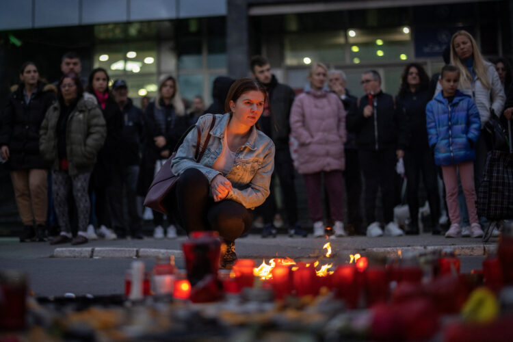 Ljudje prižigajo sveče in nosijo cvetje pred železniško postajo v Novem Sadu